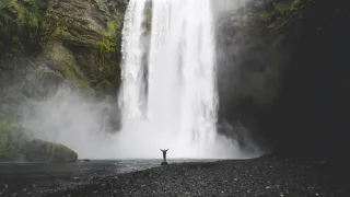 A huge waterfall in the background and a small figure standing at the bottom, raising their arms.