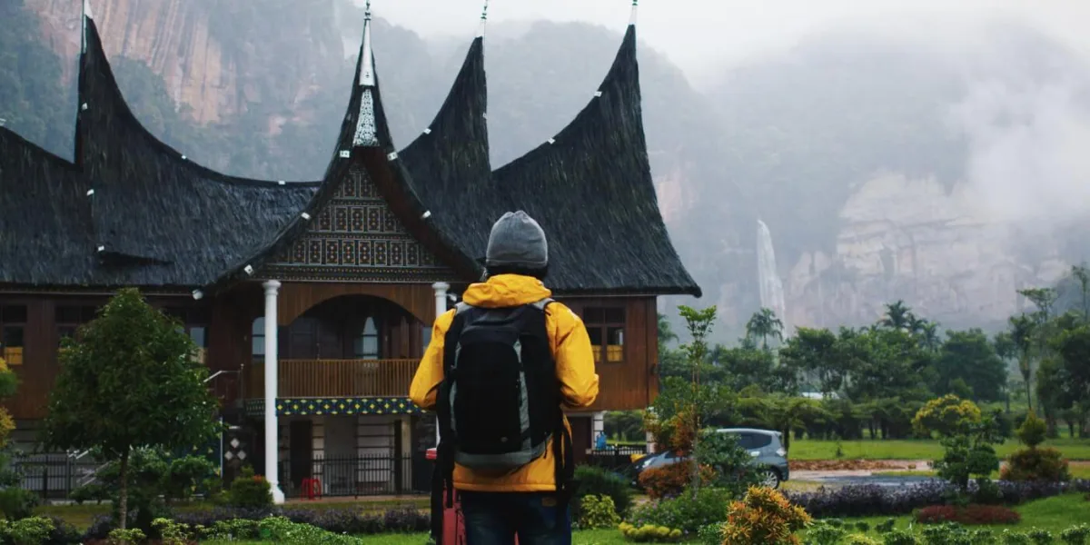 A hiker stands in front of an old asian building. Misty mountains in the background.